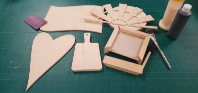 A picture of some wood craft supplies ready to be decorated. Includes a stencil, paint brushes, some black paint, and wood glue.